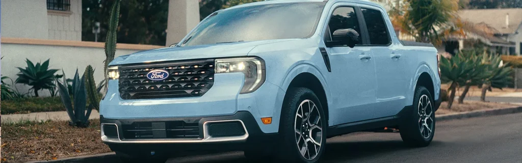 Light blue Ford Maverick pickup driving through a residential neighborhood.